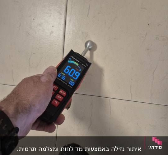 מד לחות על רצפה, יד מחזיקה את המכשיר